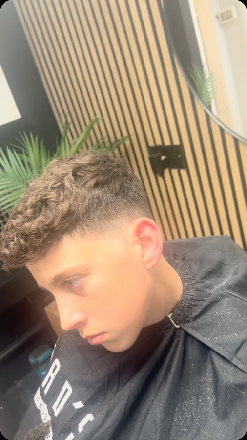 Curls left full on top over a tight fade.