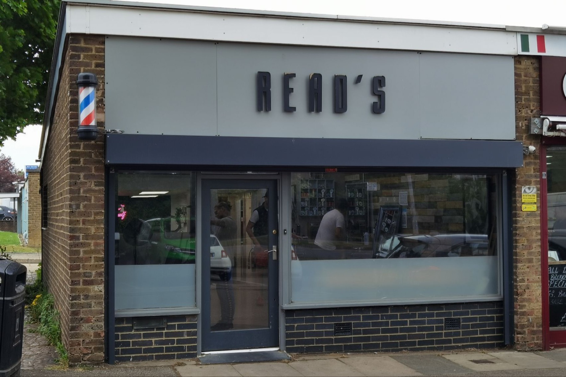 The Read's Barbers shopfront on the Mill Hatch parade: a pale grey fascia with dark raised letters reading READ'S, a charcoal awning and a traditional barber pole.